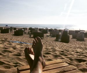 Low section of woman resting on deck chair at beach against sky