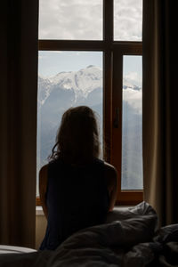 Rear view of woman looking through window at home