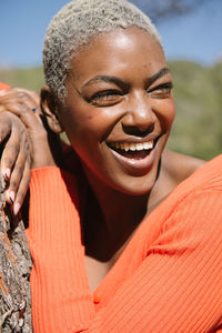 Cheerful african american female with platinum short dyed hair standing near tree trunk and observing environment