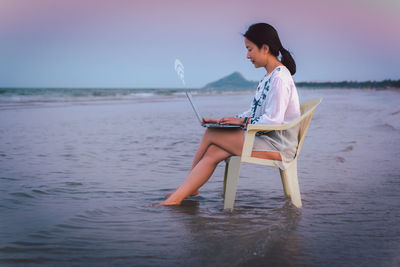 Side view businesswoman using laptop while sitting in a chaie on the beach