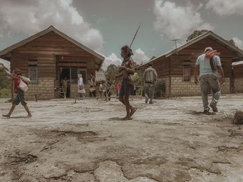 People walking outside house against sky