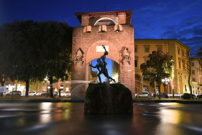 Statue by illuminated buildings against sky at night