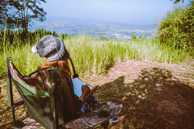 Woman with diary sitting on chair against landscape