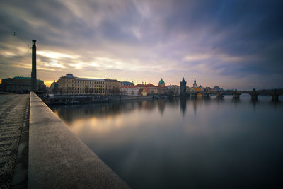 Bridge over river by buildings against sky during sunset