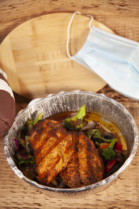 Grilled chicken in takeout container with  broccoli, onions, football,   wooden football, and  mask