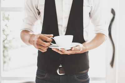 Midsection of man holding coffee cup against door