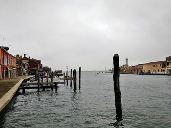 Wooden posts in sea by buildings against sky