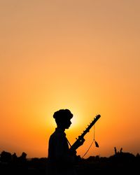 Silhouette man standing against orange sky during sunset