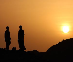 Silhouette men standing on landscape against orange sky