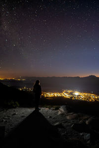 Rear view of man standing on mountain against sky at night