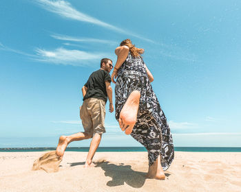 Low angle view of couple running at beach against sky
