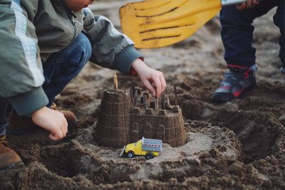 Low section of boy making sand castle by brother at beach