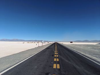 Road leading towards mountains against clear blue sky