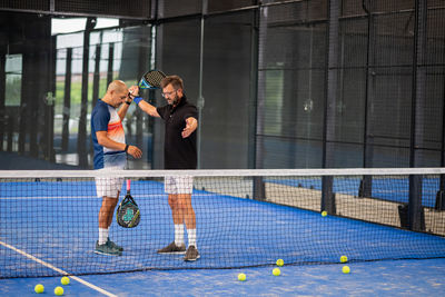 Monitor teaching padel class to man, his student - trainer teaches boy how to play padel on indoor 
