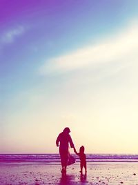 Rear view of woman standing at beach against sky during sunset