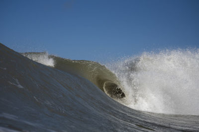 Waves splashing on shore against clear sky