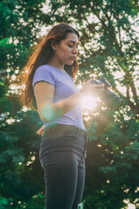 Young woman looking away while standing against trees