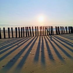 Wooden posts on beach against sky during sunset