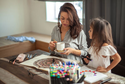 Mother and daughter drawing while sitting at home