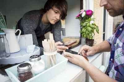 Midsection of male customer paying through card reader while owner holding digital tablet at food truck