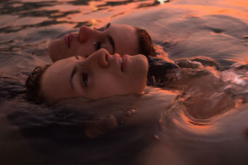 Close-up of friends relaxing in lake during sunset