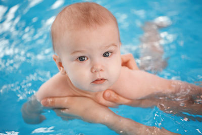 Cropped hands of woman holding baby boy in swimming pool