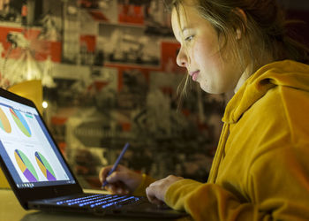 Side view of teenage girl using laptop on table at home