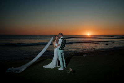 Wedding couple standing on beach against sky during sunset