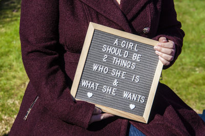 Midsection of woman holding slate with text outdoors
