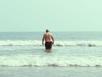 Rear view of shirtless man in sea against clear sky