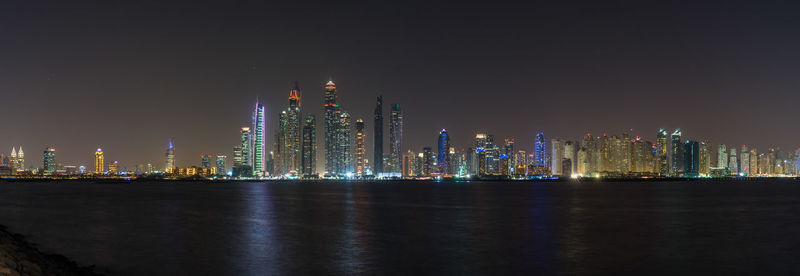 Illuminated buildings by river against sky at night