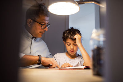 Father and son reading book in darkroom at home