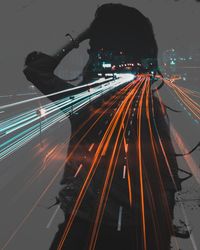 Double exposure of woman and light trails on road at night