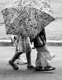 Low section of siblings walking with floral umbrella on street