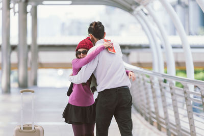 Smiling woman embracing boyfriend on elevated walkway at airport