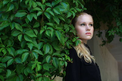 Close-up portrait of young woman standing against plants