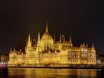 Illuminated hungarian parliament building by river against sky at night