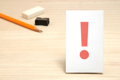 High angle view of exclamation point on paper with pencil and eraser on wooden table