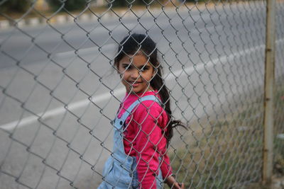 Portrait of girl standing by chainlink fence