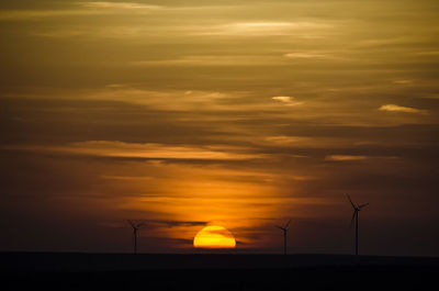 Wind turbines on landscape against cloudy sky