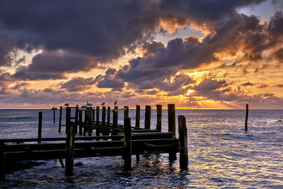 Wooden posts on beach against sky during sunset