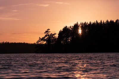 Silhouette trees by lake against sky during sunset
