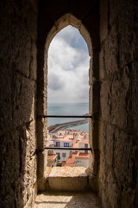 Buildings by sea against sky seen through window