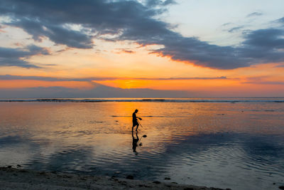 Silhouette of person walking on beach at sunset