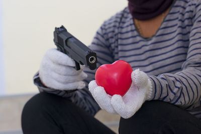 Midsection of burglar aiming handgun on heart shape against wall