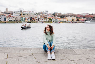 Young beautiful woman sitting by the river at sunset enjoying porto views. travel concept