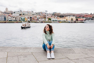 Portrait of smiling woman sitting by river in city