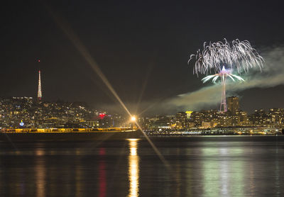 Firework display over river and illuminated buildings in city at night