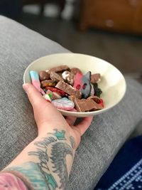 Cropped tattooed hand holding food in bowl at home