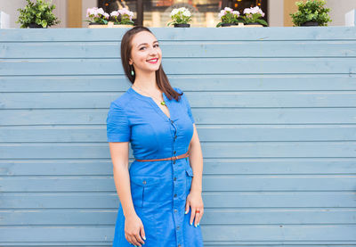 Portrait of smiling young woman standing against blue wall